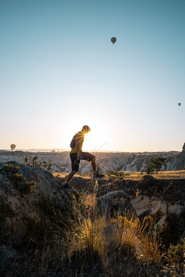Homem subindo uma rocha ao entardecer com balões ao fundo, simbolizando a superação de obstáculos e a busca por novos horizontes